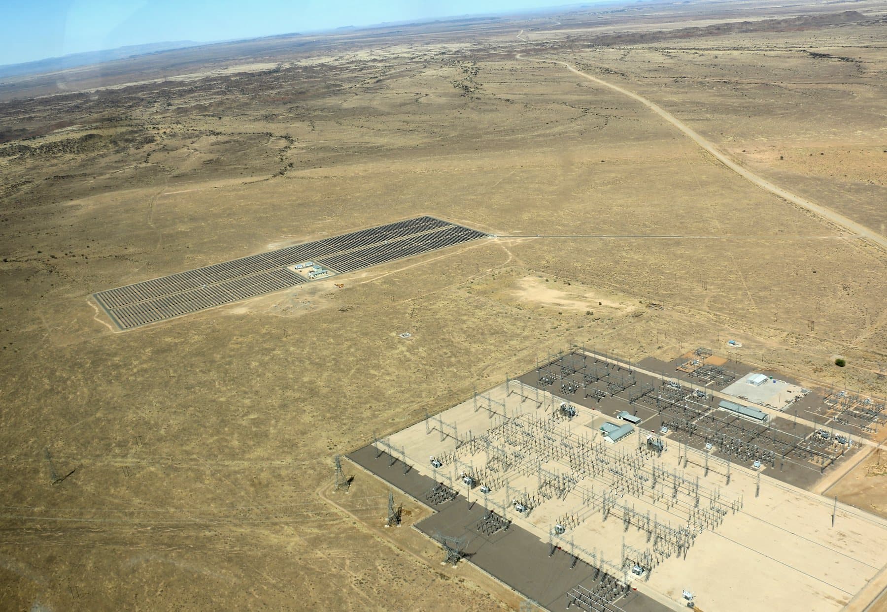 Aerial view of a photovoltaic array beside the Kokerboom high-voltage substation on open ground.